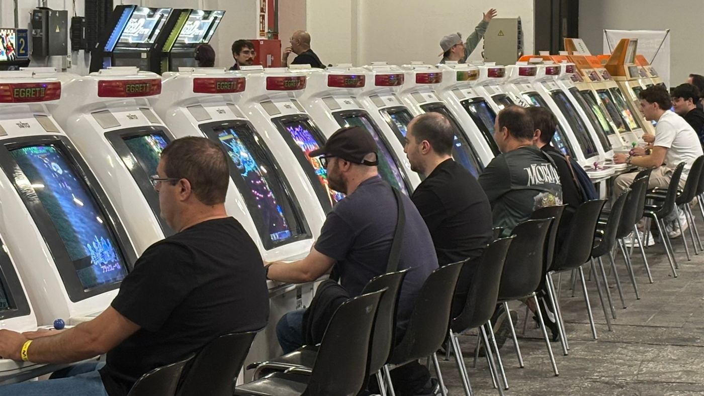 Players seated in a row at white Taito Egret II arcade cabinets.